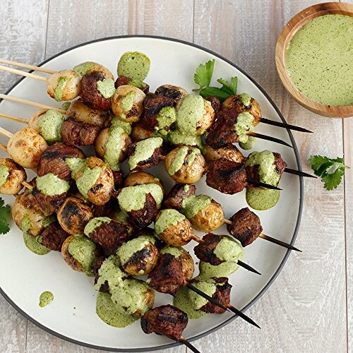 Grilled skewers with meat and vegetables drizzled with green sauce on a plate.