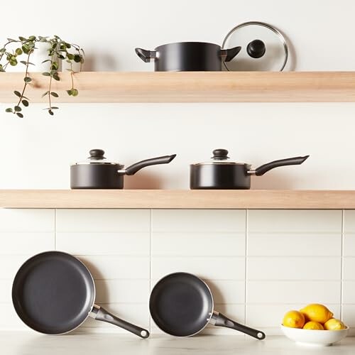 Cookware set including pots and pans on kitchen shelves with a bowl of lemons.