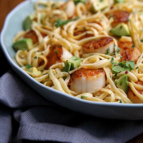 Linguine pasta with seared scallops and avocado garnished with herbs.