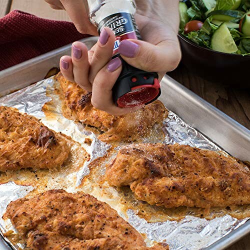 Person seasoning baked chicken breasts on a tray.